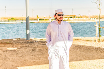 Front view of Saudi Arabian man, in traditional dress, walking in a maritime area.