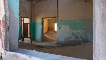 Inside of a sandfilled room at one of the houses framed by a windowframe at the ghost town of Kolmanskop, Namibia