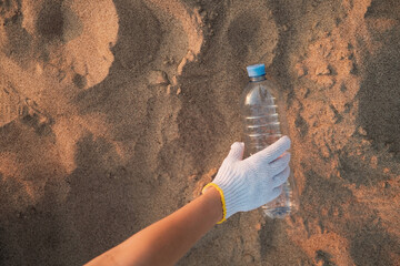 A man collects a used plastic bottle on a sandy beach. Environmental problem of plastic waste...