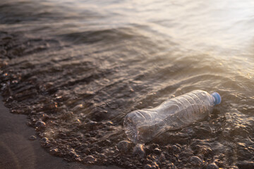 An empty plastic bottle floats in the water near the shore. The water reflects the sun's rays. Environmental problem of pollution of reservoirs with plastic waste.