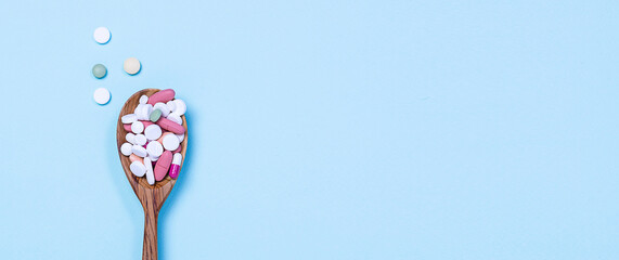 Assortment of medical pills and tablets in the wooden spoon on light blue background. Long banner format. Health care concept.
