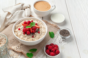White bowl with oatmeal porridge with berries and chia seeds. A healthy breakfast. Side view, copy space.