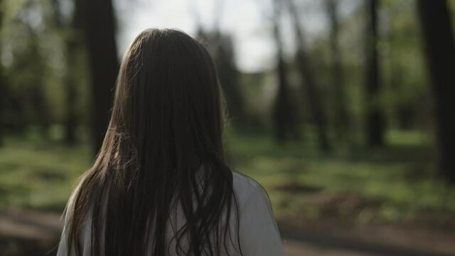 Slow motion shot of young woman walk and turn around in a park on a sunny summer day