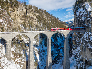 Filisur Zwitserland - 31 januari 2019: Een rode Zwitserse passagierstrein passeert het beroemde Landwasser Viaduct - een luchtfoto per drone