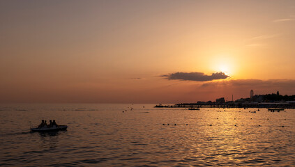 Red sunset over the dark evening sea, where there are many people swimming. Summer landscape