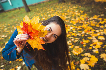 Playful young woman with autumn leaves in hand and fall yellow maple garden background