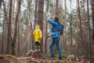 Mom and child walking in the forest after rain in raincoats together, looking at the sky