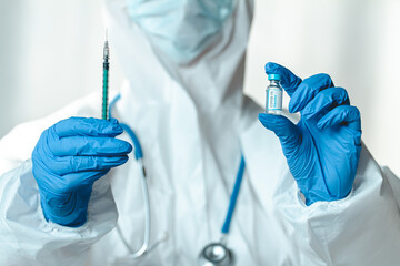 Doctor or nurse in a protective suit holds a syringe and covid 19 vaccine