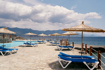 Fototapeta na wymiar Sun loungers stand under a beach umbrellas near pool