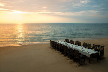 Fototapeta premium Table setting for a romantic festive dinner at sunset on the sea. Wedding or celebrating decoration