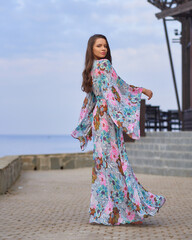 Full length outdoor portrait of young elegant tall woman in colorful blue dress with floral print...
