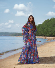 Elegant woman in colorful tunic standing and posing at sandy beach on s ummer sunny day.