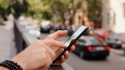 Male hand with bracelet using smartphone closeup in the summer city