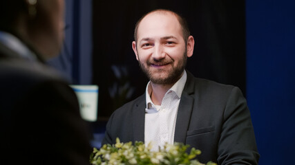 Portrait of focused manager looking into camera sitting at conference table in meeting office room late at night. Diverse multi ethnic business coworkers brainstorming company ideas in evening