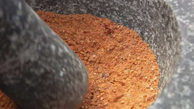 Close-up of heavy pestle grinding and mixing spices, peppers and sea salt