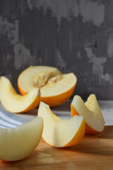 slices of fresh juicy ripe yellow melon on a wooden board with half a melon in the background