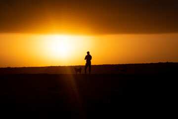 Young Man next to a Dog are Looking the Sunrise in the Desert at Punta Gallinas, with a Yellow Sky Full of Clouds in La Guajira, Colombia