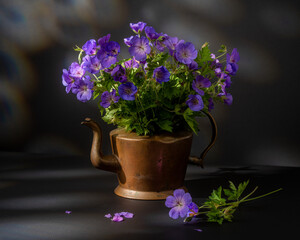 Fototapeta premium Still life on a table with flowers, books, tea pot and dark background