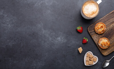 Ceramic mug with coffee, tasty cakes and strawberries on dark stone background. Top view. Copy space