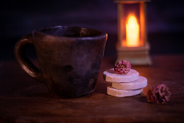golosina de almendra acompañada de una taza de café y una luz de vela al fondo sobre una base de madera antigua 