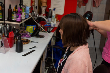 Portrait of young girl in hair salon while female hairdresser is drying her hair