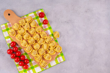 Uncooked tortelloni with mushroom filling on a wooden board.