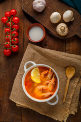 Tom yam soup with shrimps and coconut milk on a table on wooden boards near milk mushrooms and tomatoes.