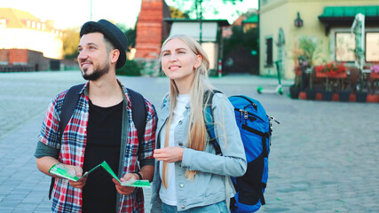 Trendy couple of tourists finding necessary destination on map and admiring surroundings. They standing on city square.