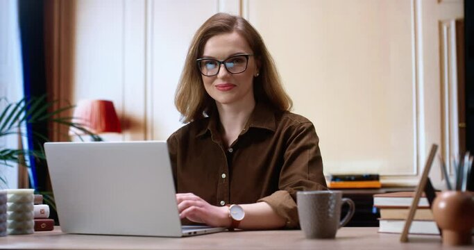 Brunette woman wearing casual clothes working on internet. Woman is looking to the camera and using laptop computer. Picture showing pretty woman working and rejoicing