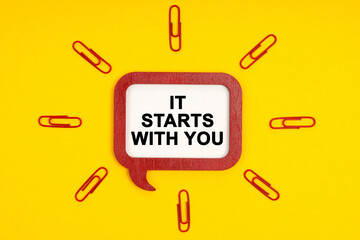On a yellow background, paper clips and a mental plaque with the inscription - It Starts With You