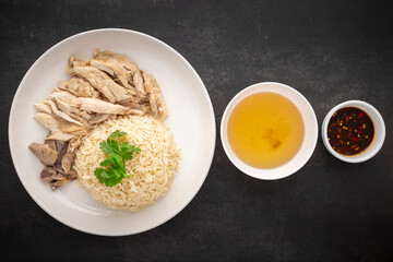 Khao Mun Gai, Thai food, rice steamed with chicken soup serve with chicken, soup and sauce on dark tone texture background, top view