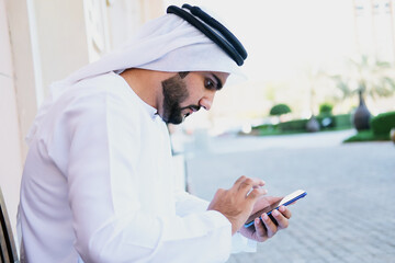 Arab man waiting car service through smart moble phone app. Arabic man checks the update status of his transporation request. Middle Eastern man on kandura using cellphone