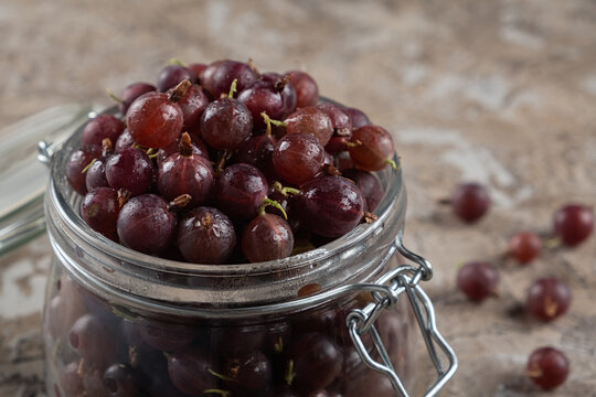 Ripe gooseberry berries of burgundy color close-up in a glass jar. Horizontal orientation, copy space, no people
