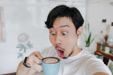 Happy Asian man enjoy his coffee and selfie himself with his coffee cup.
