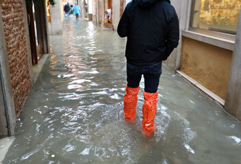 person with waterproof gaiters while walking in the street completely flooded by the high tide of...