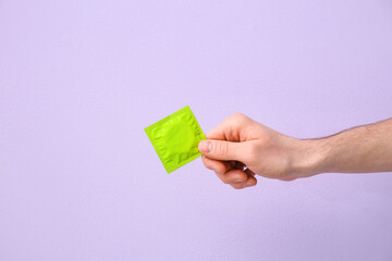 Male hand with condom on color background