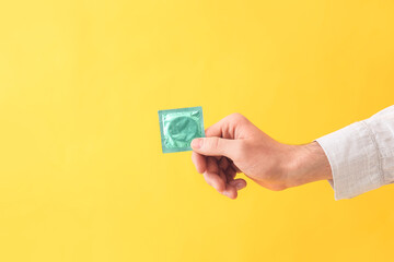 Male hand with condom on color background