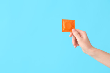 Female hand with condom on color background - obrazy, fototapety, plakaty