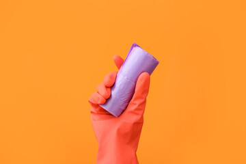 Hand in rubber glove with roll of garbage bag on color background