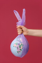 Woman holding garbage bag with globe on color background. Ecology concept