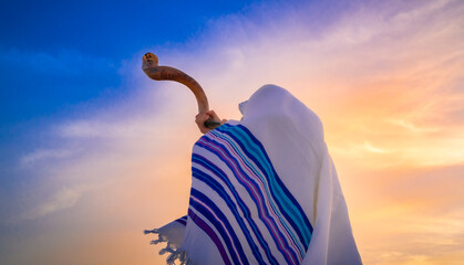 Blowing the shofar for the Feast of Trumpets - Jewish man in a traditional tallit prayer shawl blowing the ram's horn against beautiful sunset sky - obrazy, fototapety, plakaty