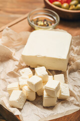 Board with delicious pieces of feta cheese on wooden background