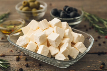 Bowl with delicious pieces of feta cheese on wooden background