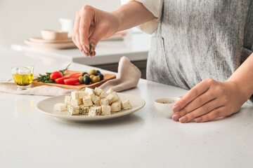 Obraz na płótnie Canvas Woman adding spices to delicious feta cheese on table