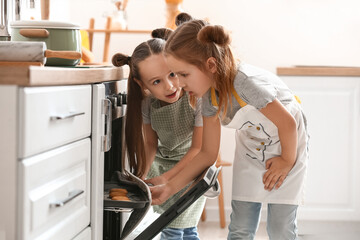 Cute little sisters taking tasty cookies from oven in kitchen