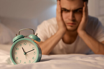 Alarm clock on bed of tired young man at night, closeup