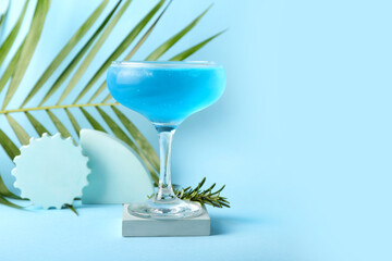 Glass of tasty cocktail and palm leaf on color background