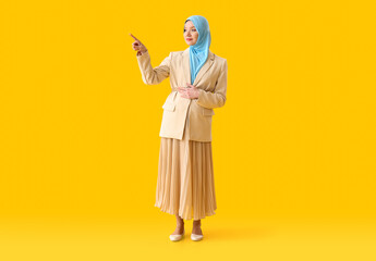 Pregnant Muslim woman pointing at something on color background