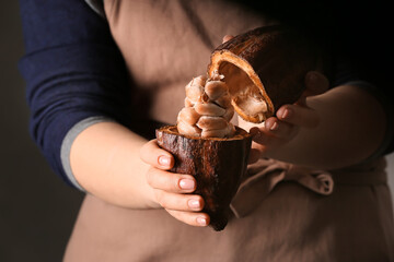 Woman holding fresh cocoa fruit on dark background, closeup