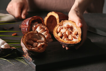 Woman holding fresh cocoa fruit on dark background, closeup